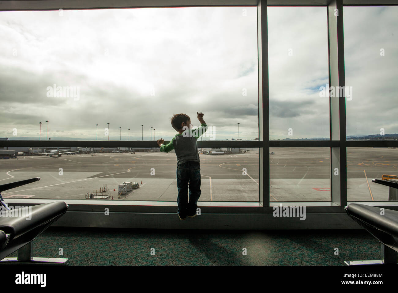 Mixed Race boy looking out window airport Banque D'Images