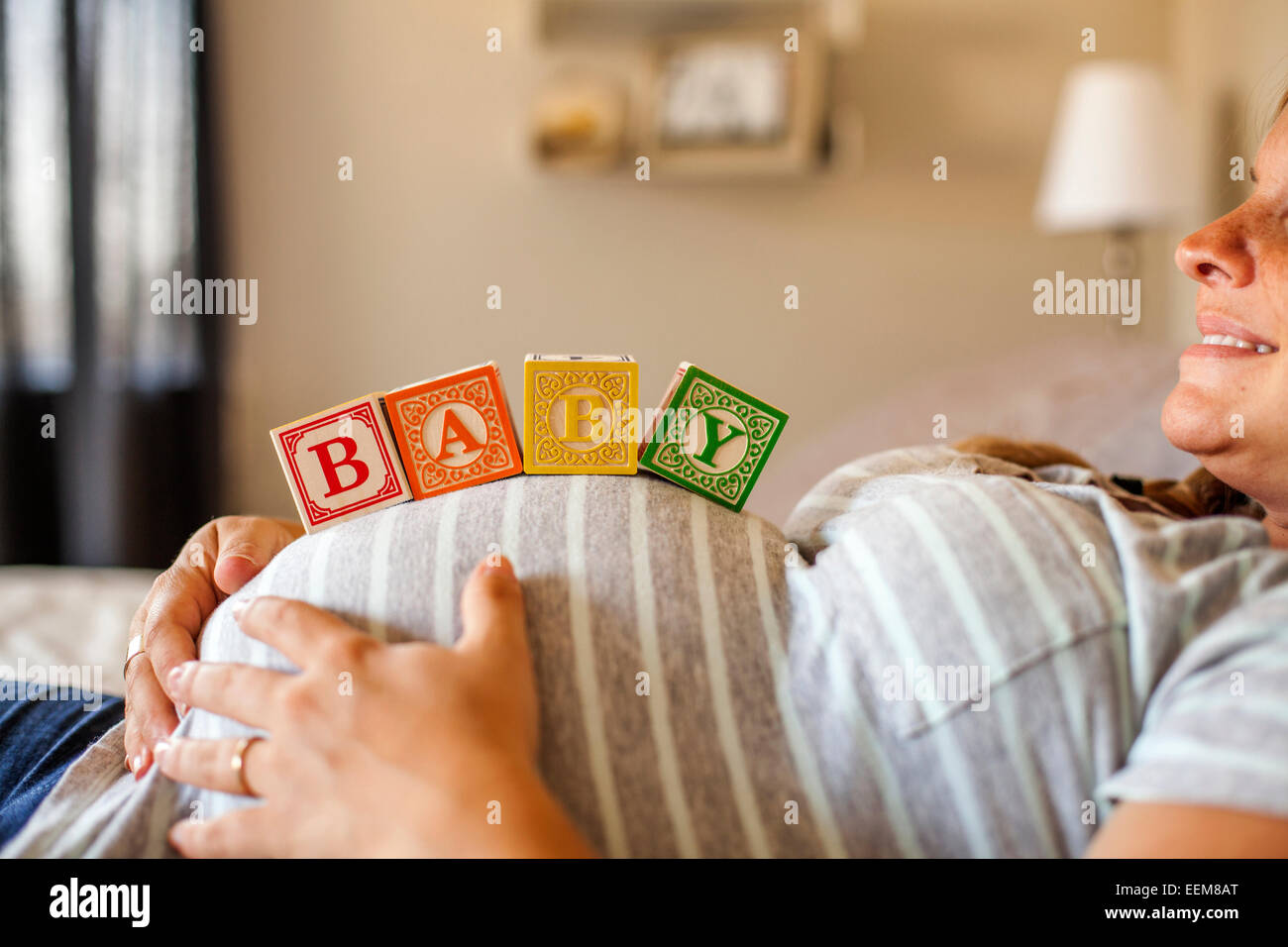 Femmes enceintes Caucasian woman balancing des blocs de bois sur son ventre au lit Banque D'Images
