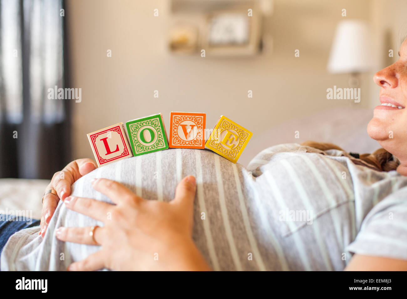 Femmes enceintes Caucasian woman balancing des blocs de bois sur son ventre au lit Banque D'Images