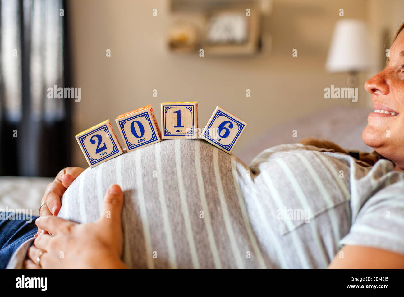 Femmes enceintes Caucasian woman balancing des blocs de bois sur son ventre au lit Banque D'Images