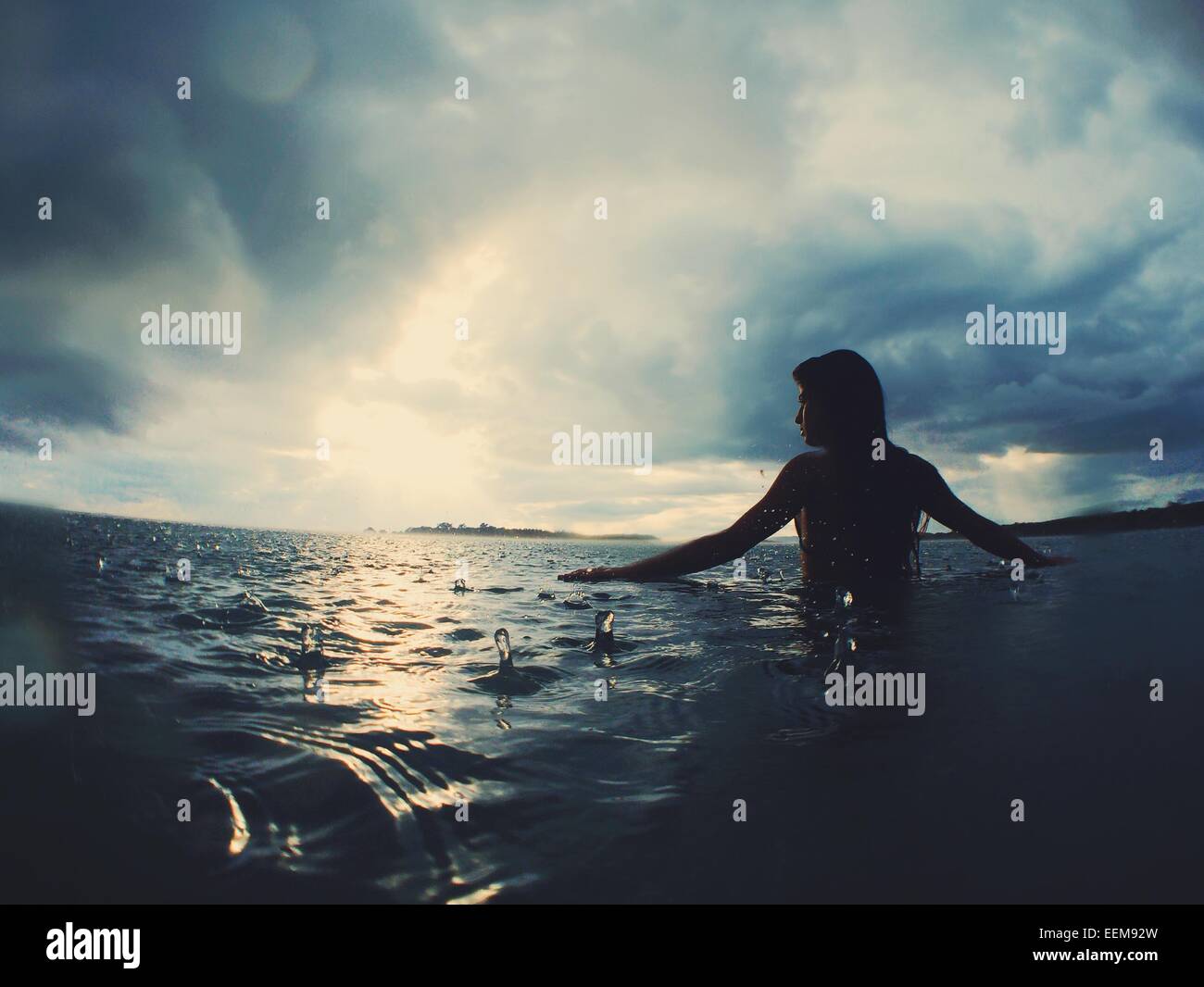 Silhouette d'une femme debout dans la mer sous la pluie Banque D'Images