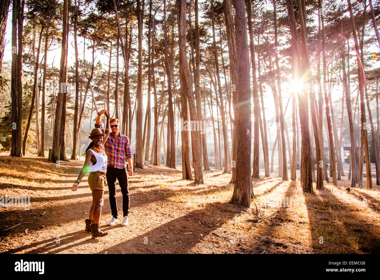 Couple holding hands sous les arbres en forêt ensoleillée Banque D'Images