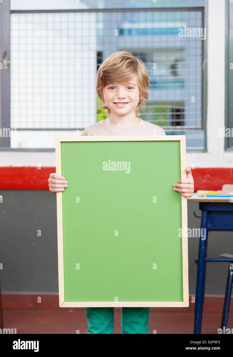 Smiling kid a l'école primaire tenue verte vide tableau. Banque D'Images