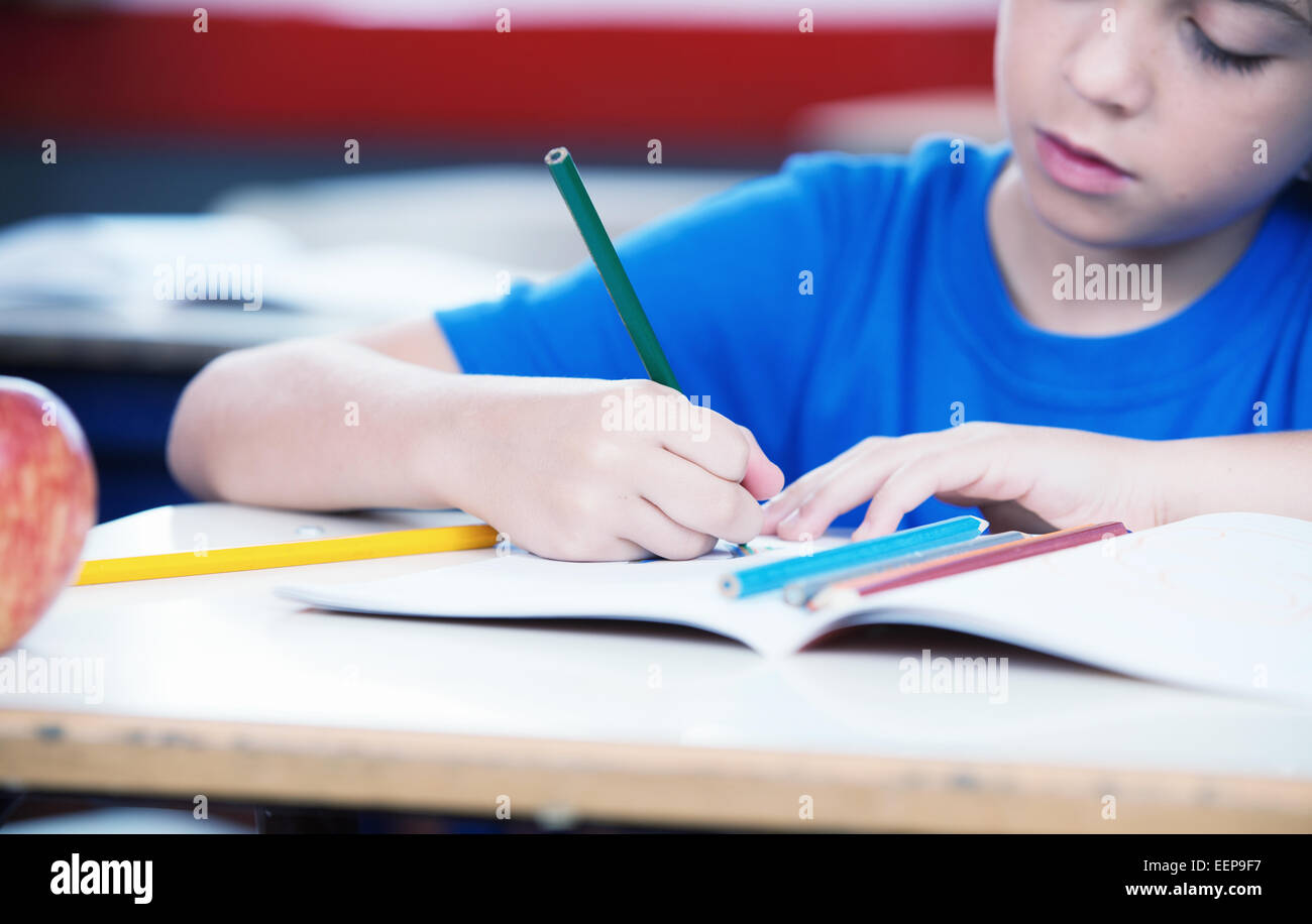 Mains d'un enfant à l'école s'appuyant sur son livre avec des crayons de couleur. Banque D'Images