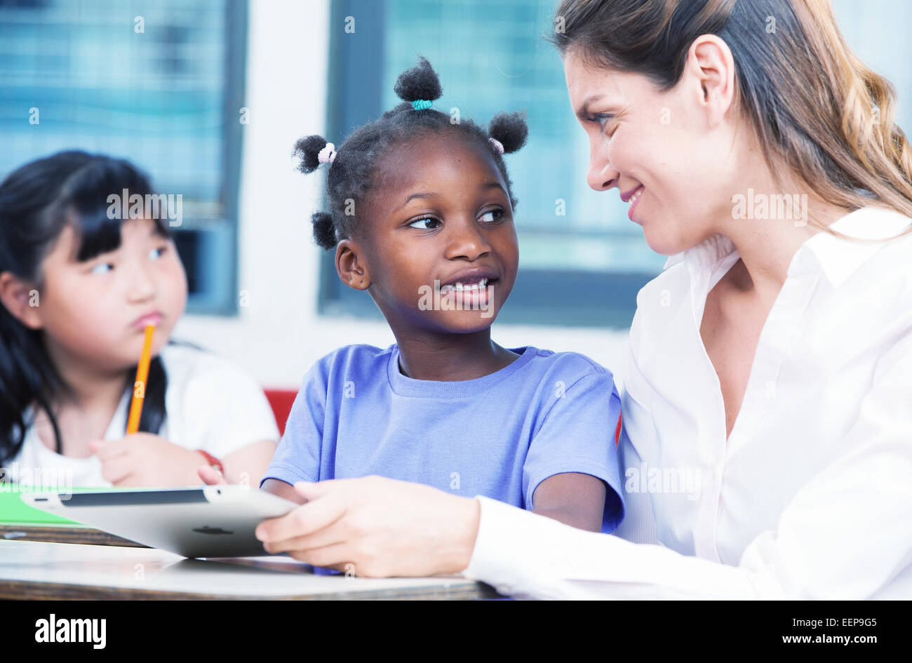 Enseignante à l'école primaire d'expliquer à afroamerican et étudiant asiatique. Banque D'Images