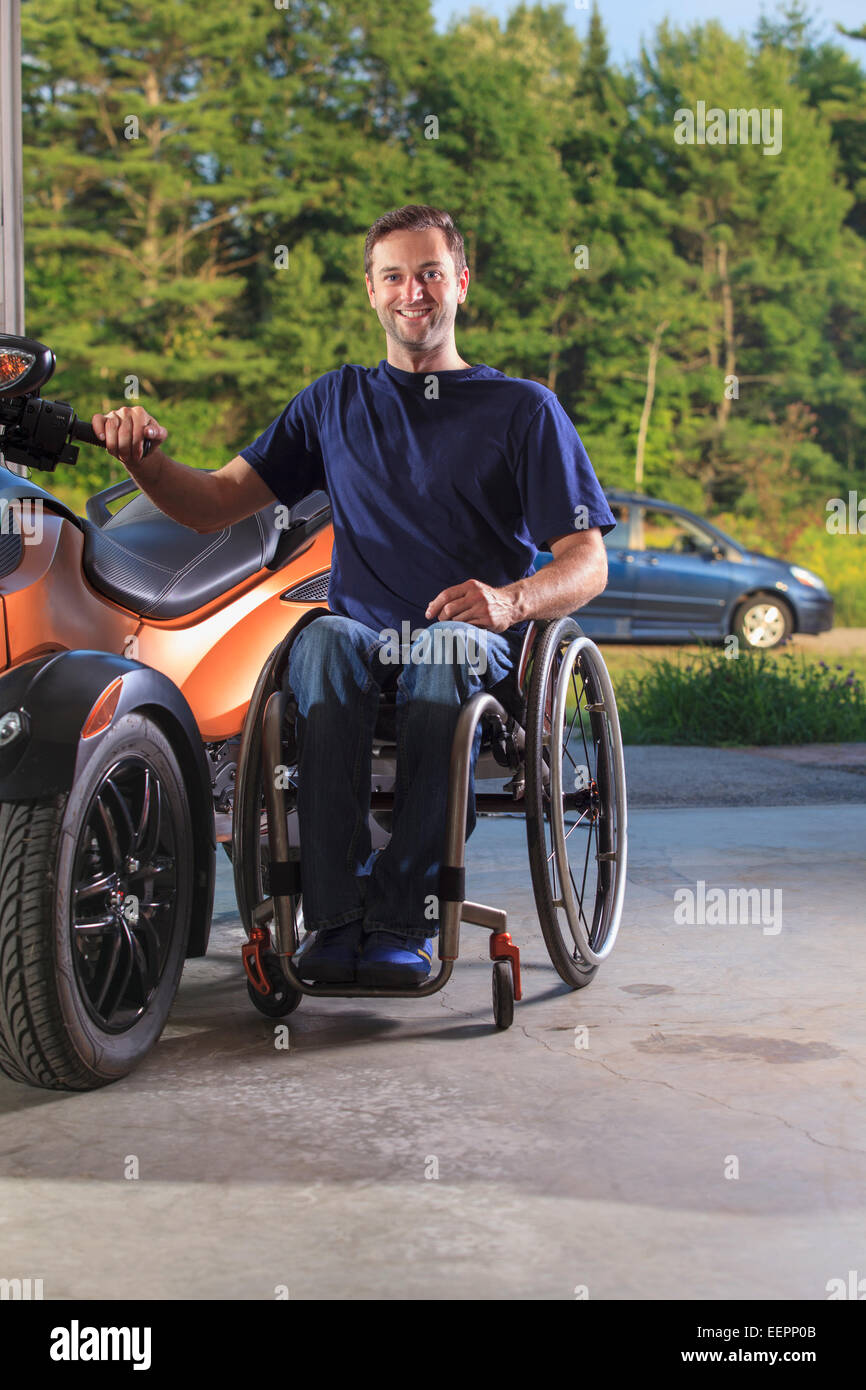 L'homme avec la moelle épinière assis à côté de son fauteuil roulant en moto custom Banque D'Images