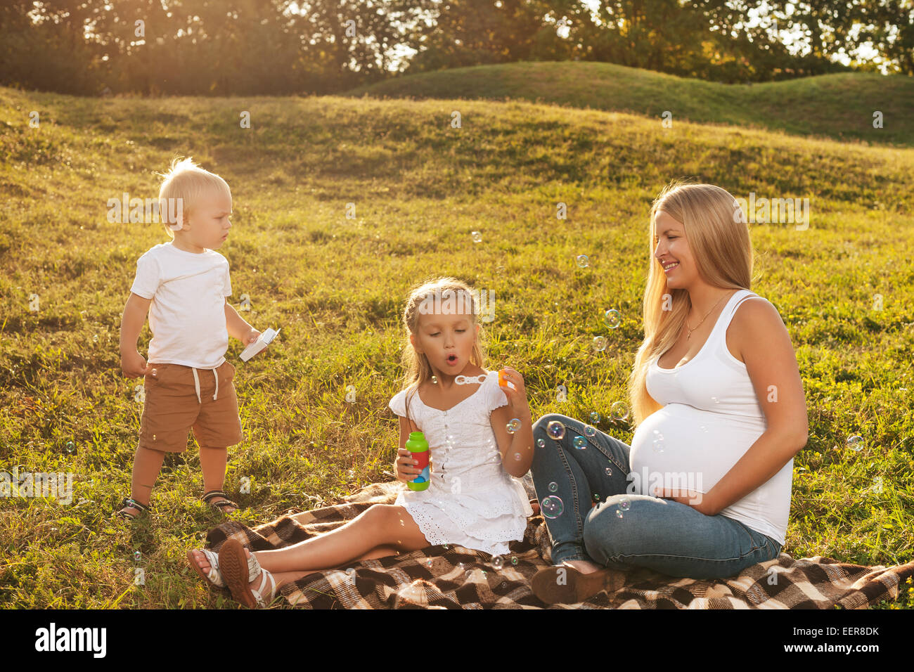 Belle blonde femme enceinte en compagnie de ses enfants plus vieux company. Mère avec des enfants en plein soleil. Concept de la fête des Mères Banque D'Images