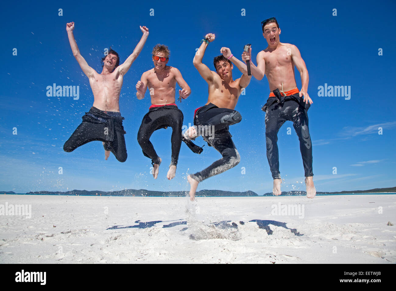 Quatre jeunes heureux de sauter en l'air sur la plage de sable blanc de Whitehaven Beach sur l'île de Whitsunday, Queensland, Australie Banque D'Images