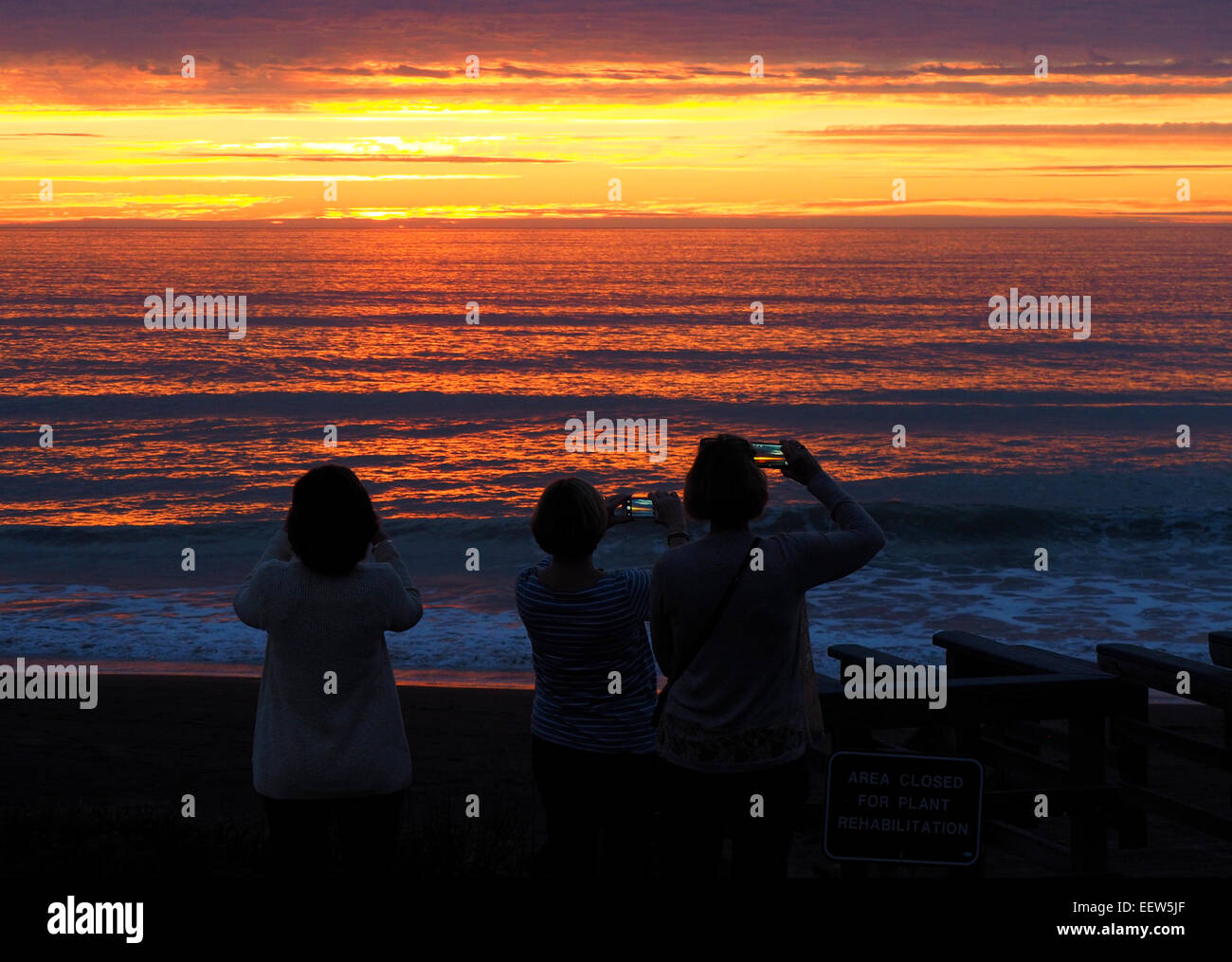 Trois femmes photographier le coucher du soleil avec un téléphone cellulaire Banque D'Images