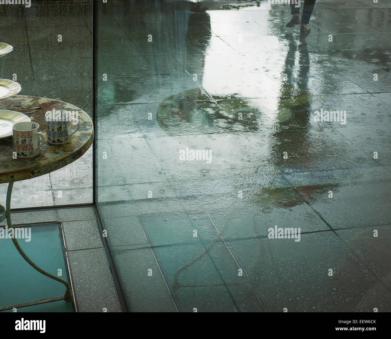 Pieds et de réflexion dans la pluie tremper trottoir de quelqu'un (femme ?) avec parapluie marche loin de table avec deux tasses. Banque D'Images