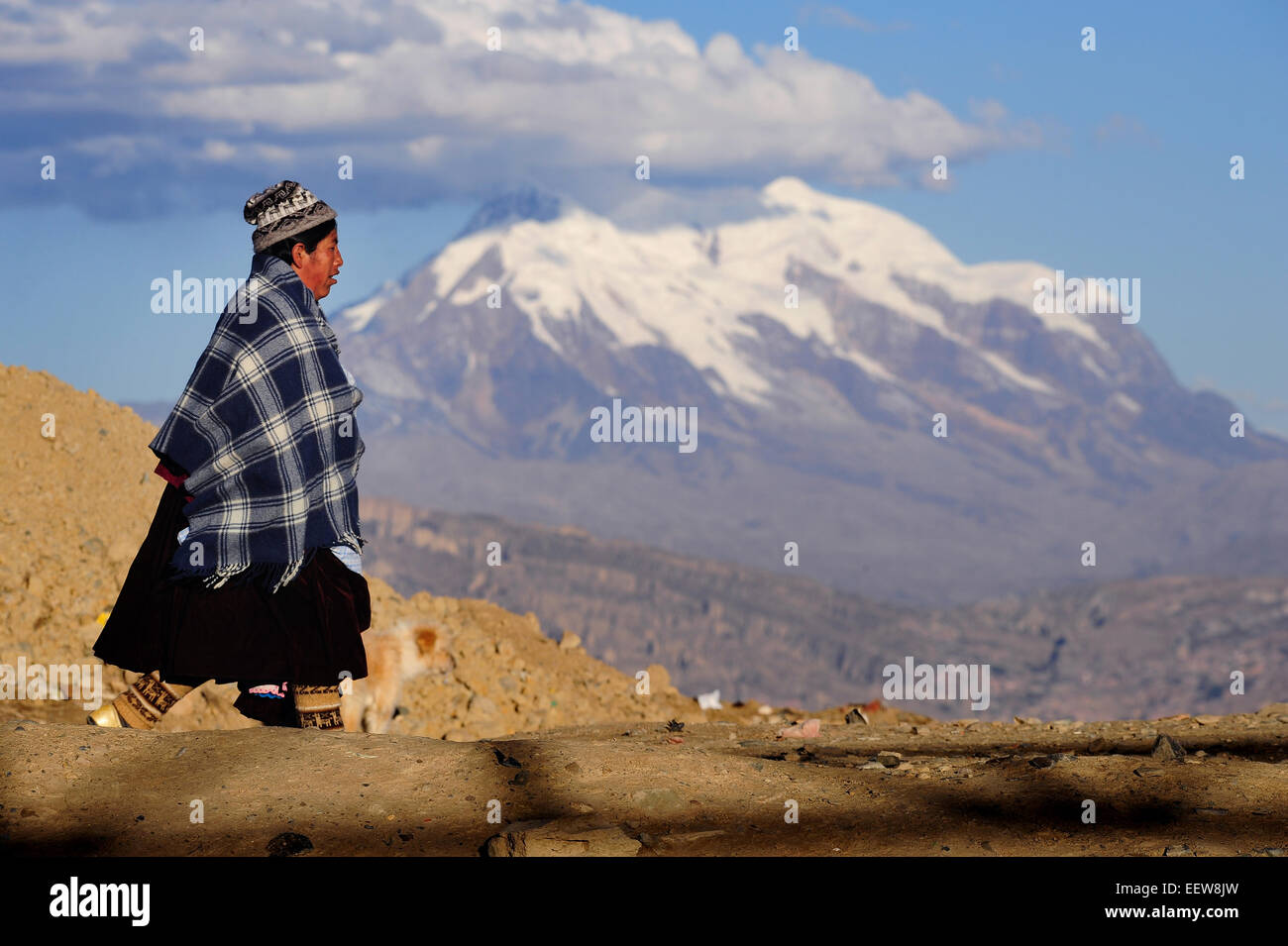 Une femme autochtone en vêtements traditionnels promenades sur un fond de la Cordillère des Andes et la deuxième plus haute montagne de la Bolivie, Illimani. Banque D'Images