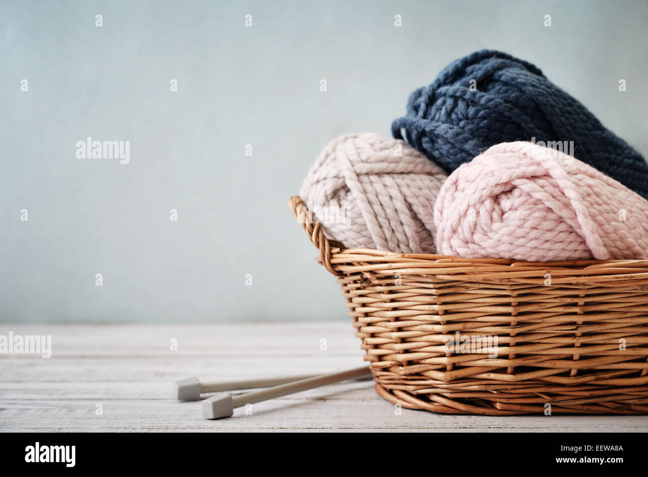 Fil de laine en rouleaux avec des aiguilles à tricoter dans le panier en osier sur fond bleu clair Banque D'Images