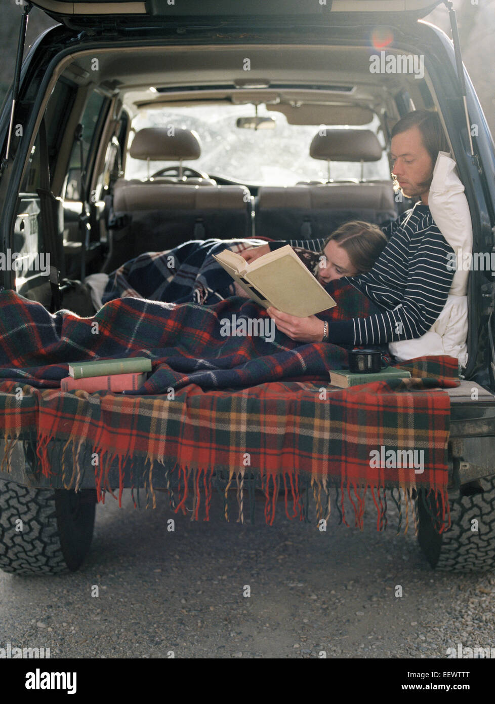Jeune couple couché dans l'arrière de leur voiture, la lecture d'un livre. Banque D'Images