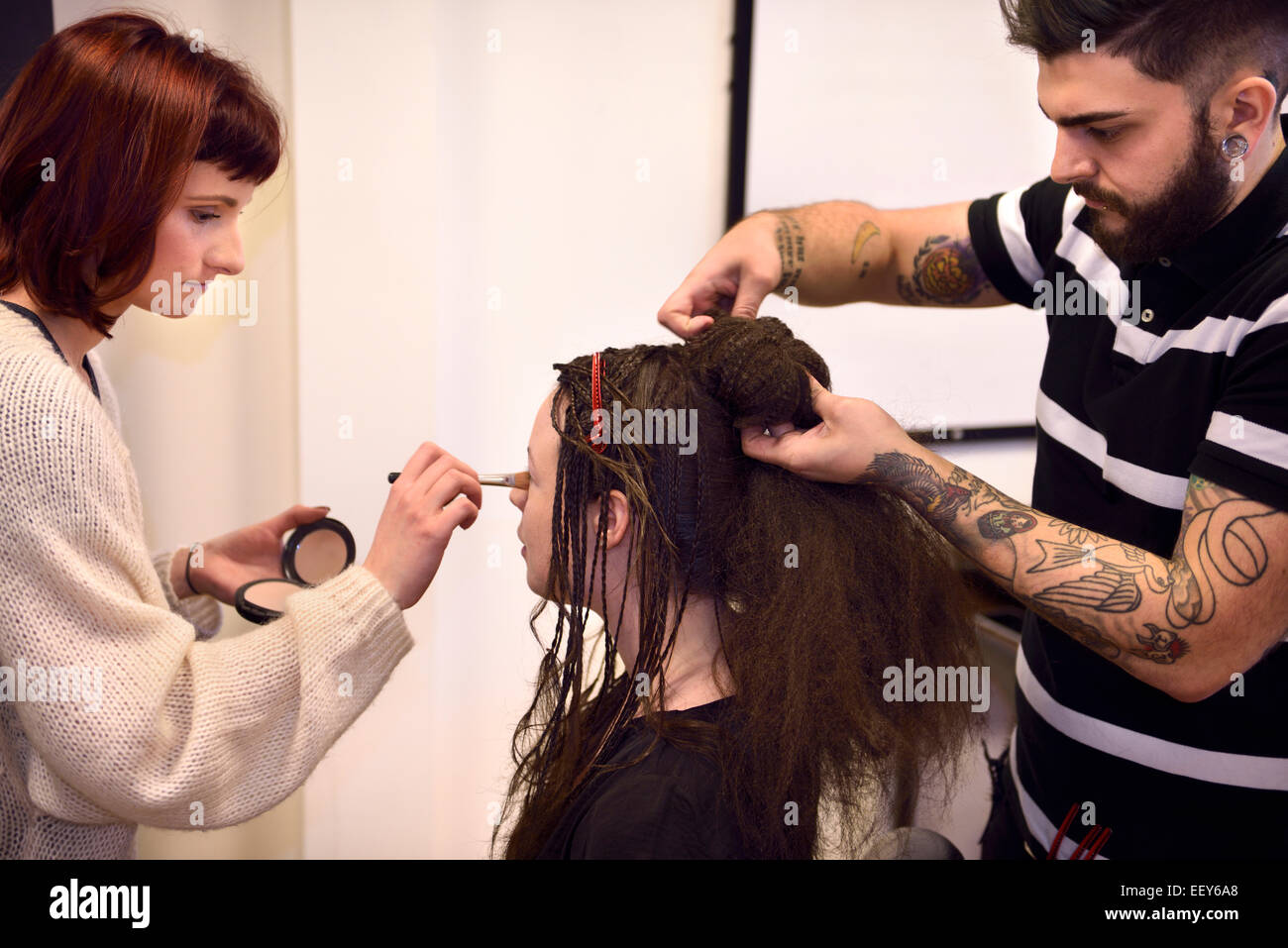 Élève maquilleur et coiffeur travaillant sur cheveux tressés avec donut sur un modèle Banque D'Images