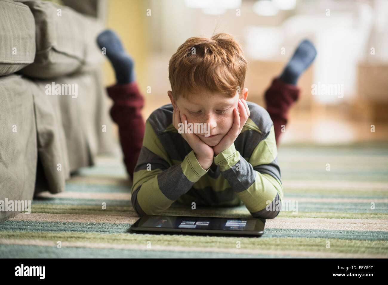 Boy (6-7) lying on carpet and using tablet pc Banque D'Images