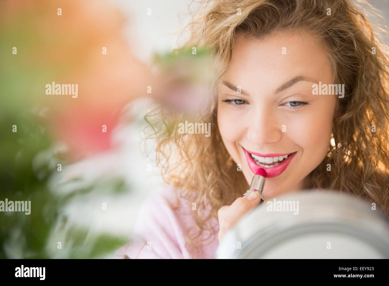 Young woman applying lipstick rouge in front of mirror Banque D'Images
