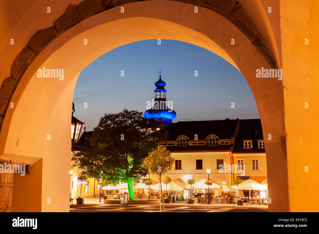 Pologne, Podkarpackie, Krosno, Allumé Place Principale avec sidewalk cafe et bulbe bleu vu par arch Banque D'Images