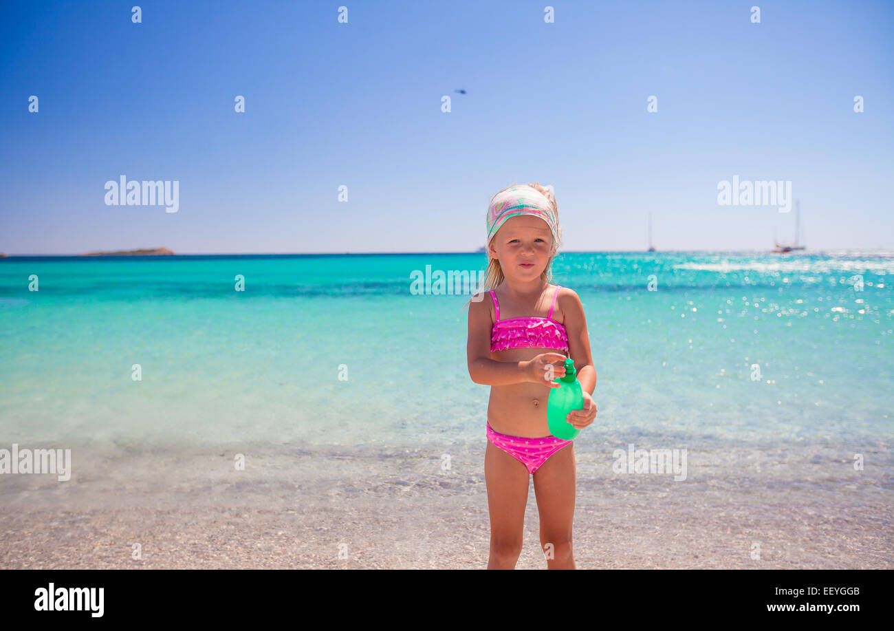 Adorable petite fille en maillot de bain avec une bouteille de lait solaire Banque D'Images