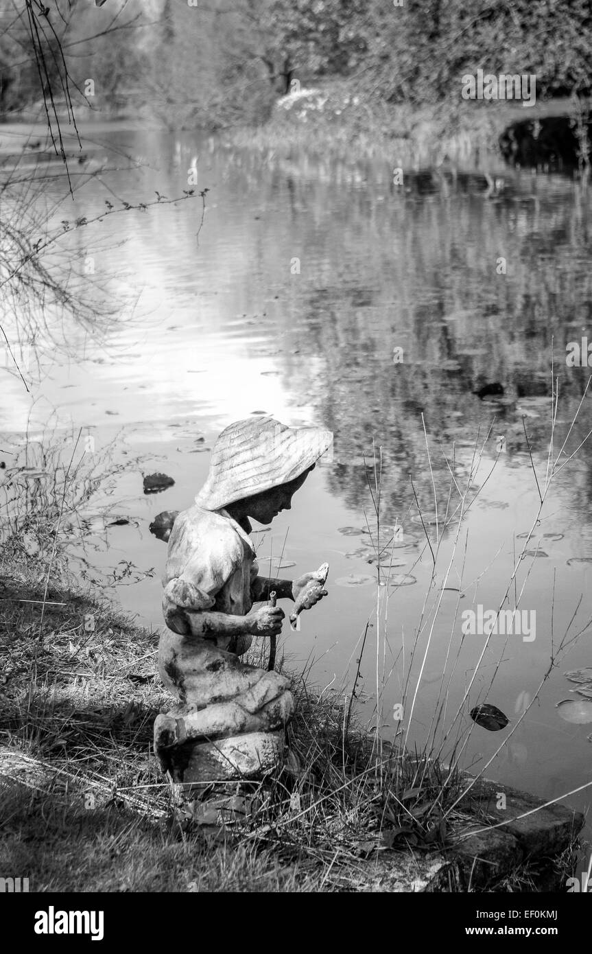 Statue de fisher boy avec des poissons en étang de jardin Banque D'Images