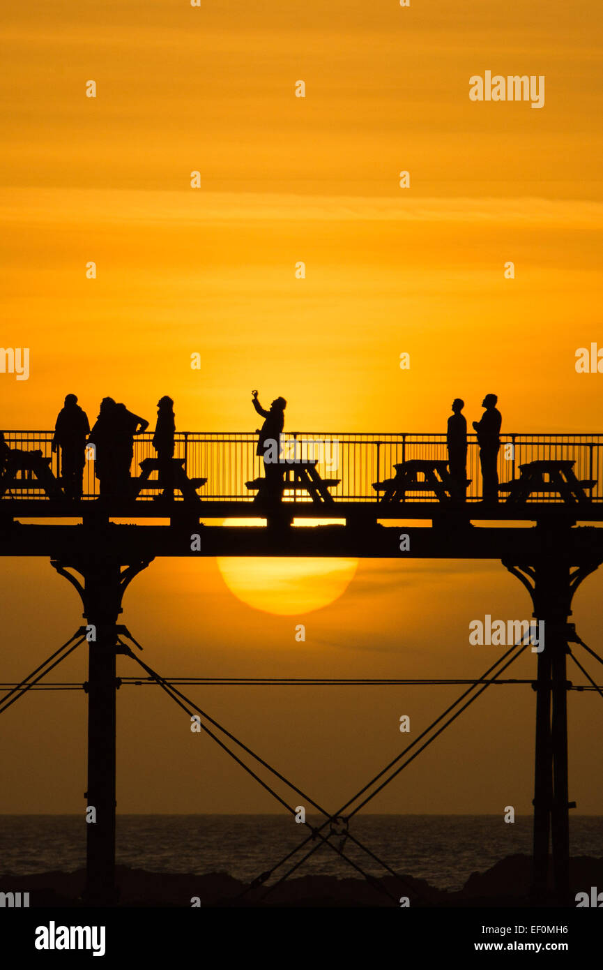 Aberystwyth, Pays de Galles, Royaume-Uni. 24 janvier, 2015. Un groupe d'ornithologues silhouette sur le coucher de soleil pendant qu'ils attendent pour voir le "urmuration' de milliers d'étourneaux volant dans le soir pour s'installer pour la nuit sur les jambes de fer de fonte de la Victorian station jetée à Aberystwyth, sur la côte ouest du pays de Galles au Royaume-Uni. La pluie à Aberystwyth est l'un des trois gîtes urbains au Royaume-Uni. Malgré leur grand nombre ici, les oiseaux sont sur la RSPB's 'list' des espèces de crédit : oiseaux britannique keith morris/Alamy Live News Banque D'Images