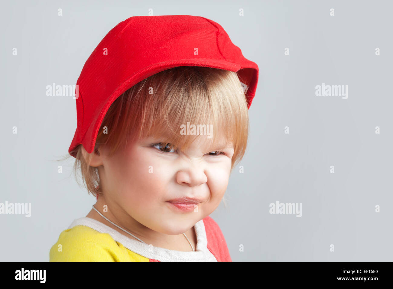 Studio portrait de funny smiling baby girl in red baseball cap sur fond de mur gris Banque D'Images