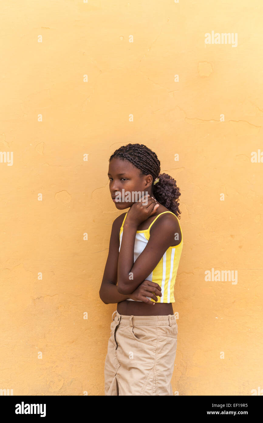 Slim réfléchie les jeunes afro-caribéenne fille cubaine de tresses, appuyé contre un mur jaune à Trinidad, Cuba Banque D'Images