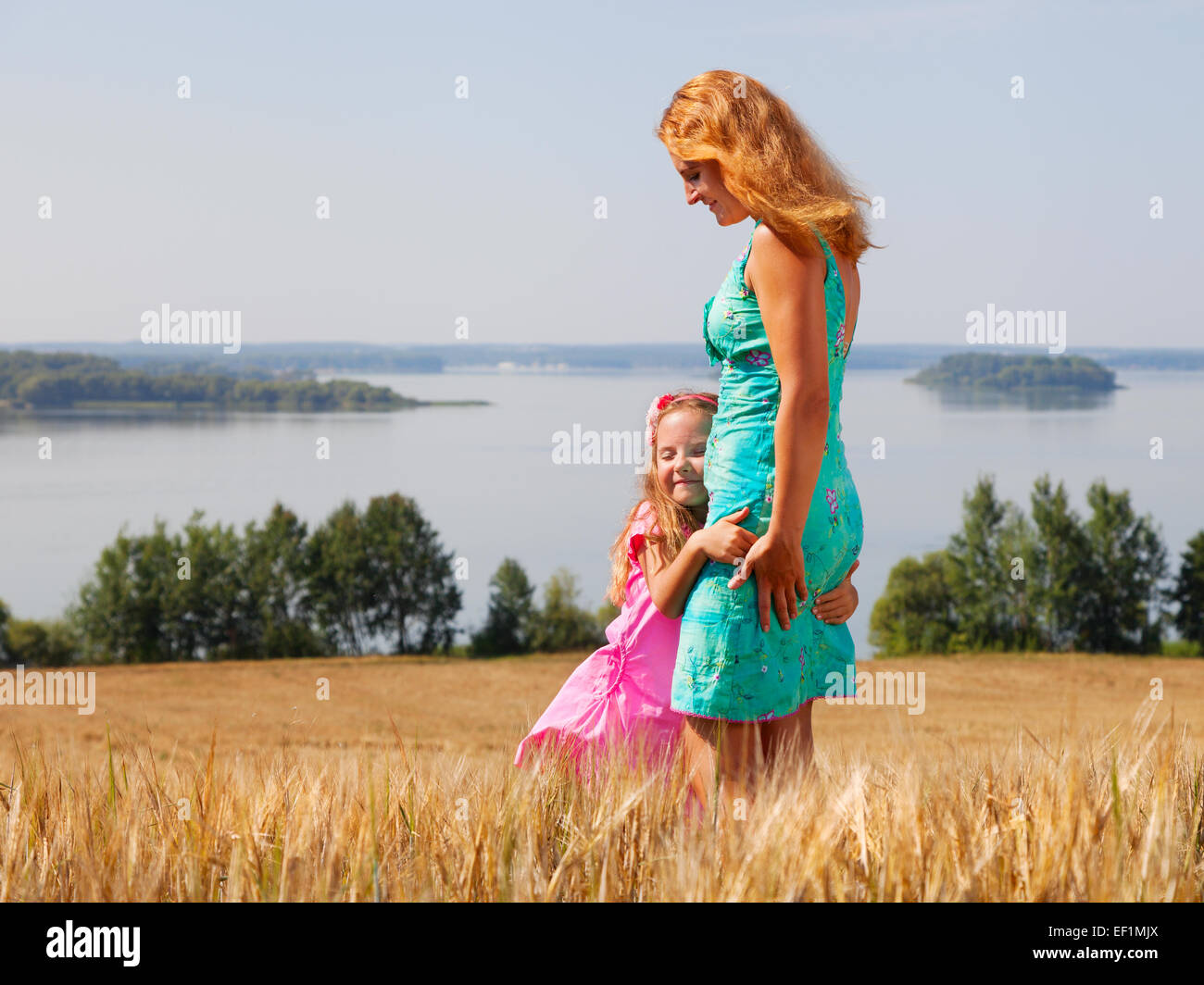 Little girl hugging sa mère dans un champ de blé près du lac sur une journée ensoleillée Banque D'Images