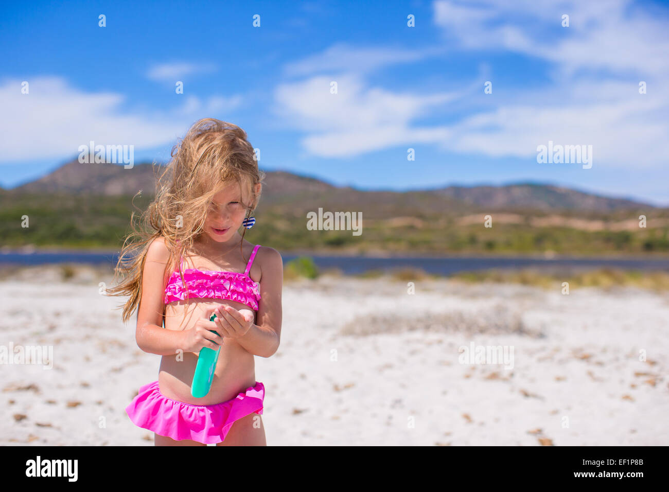 Adorable petite fille en maillot de bain avec une bouteille de lait solaire Banque D'Images