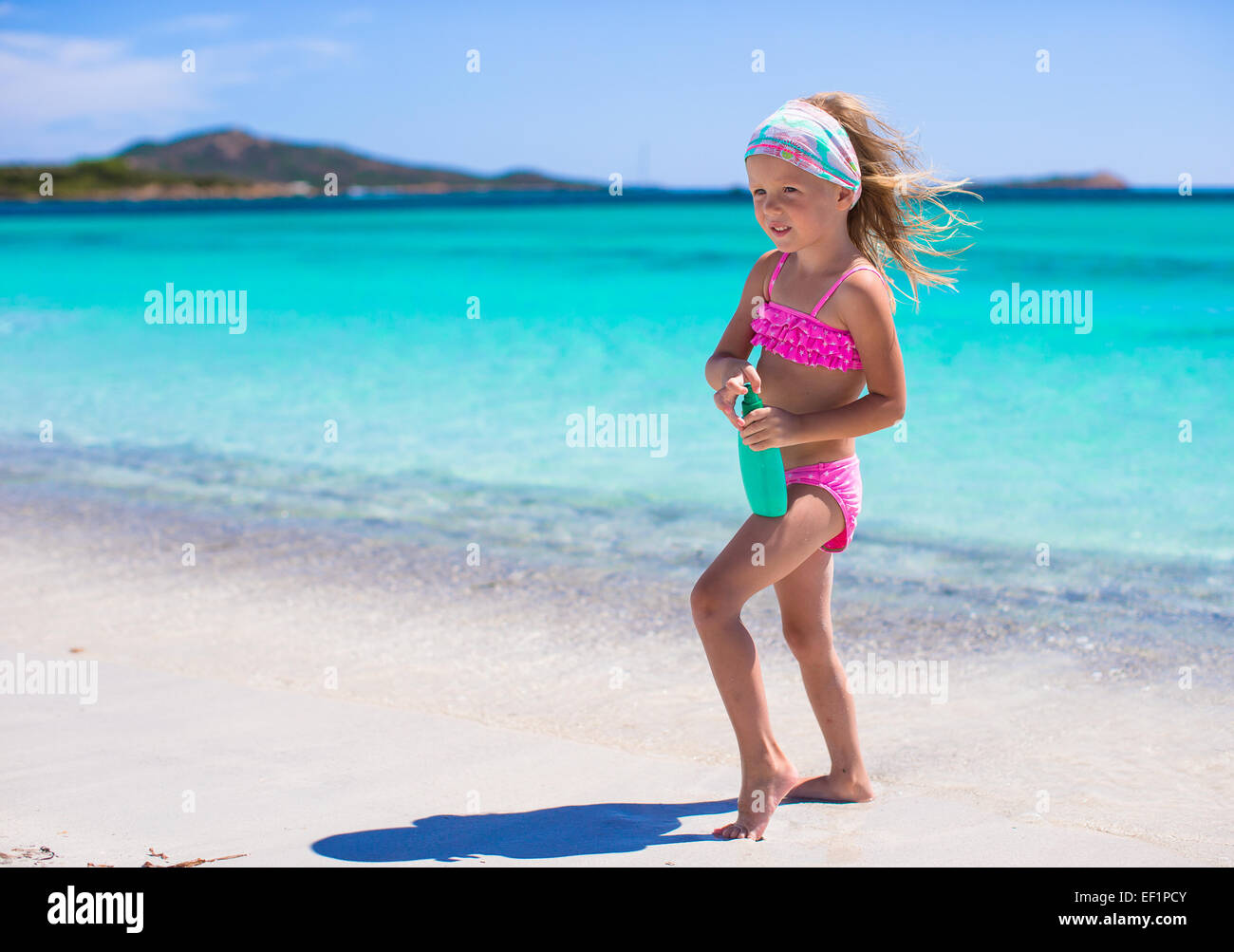 Adorable petite fille en maillot de bain avec une bouteille de lait solaire Banque D'Images