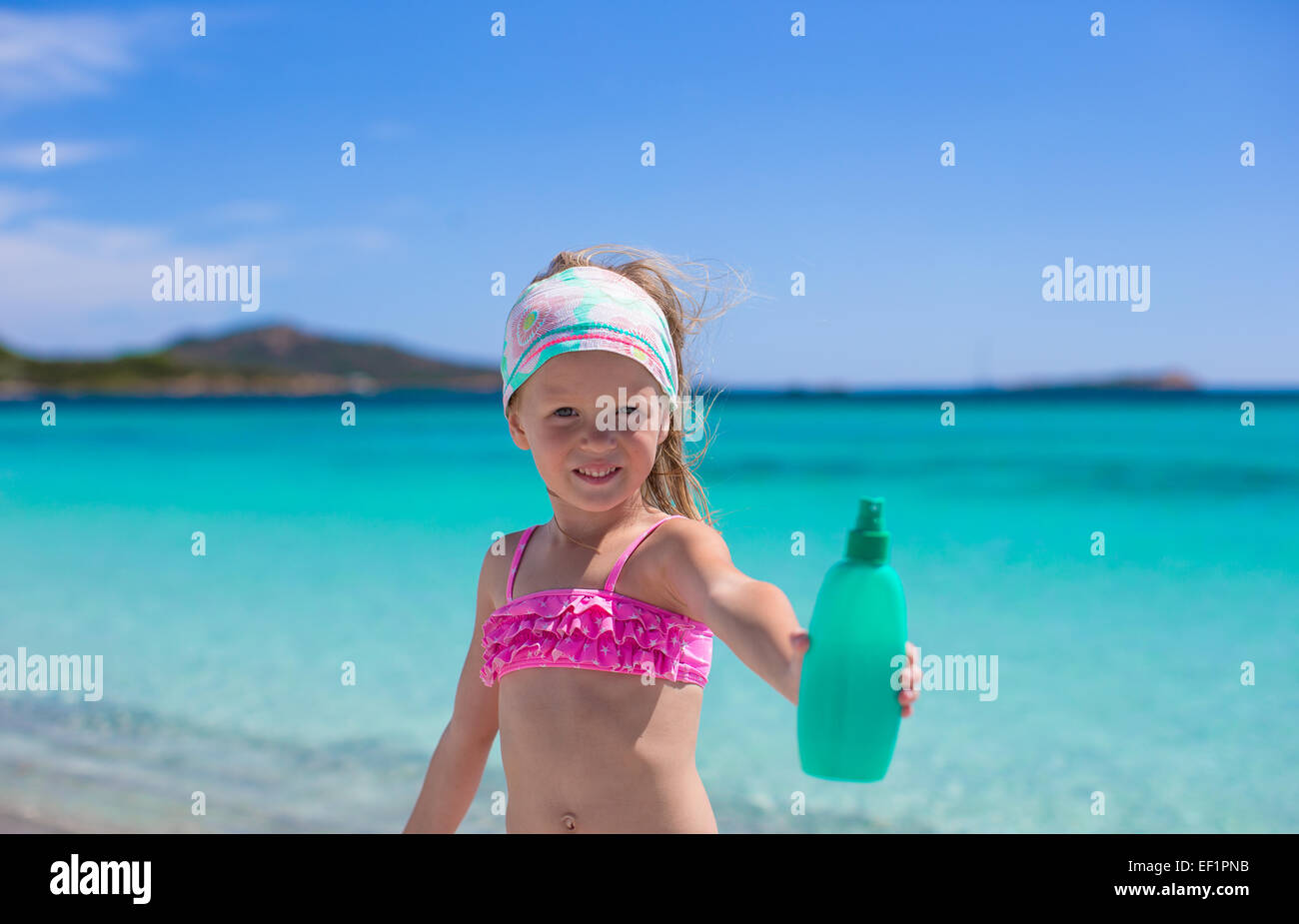 Adorable petite fille en maillot de bain avec une bouteille de lait solaire Banque D'Images