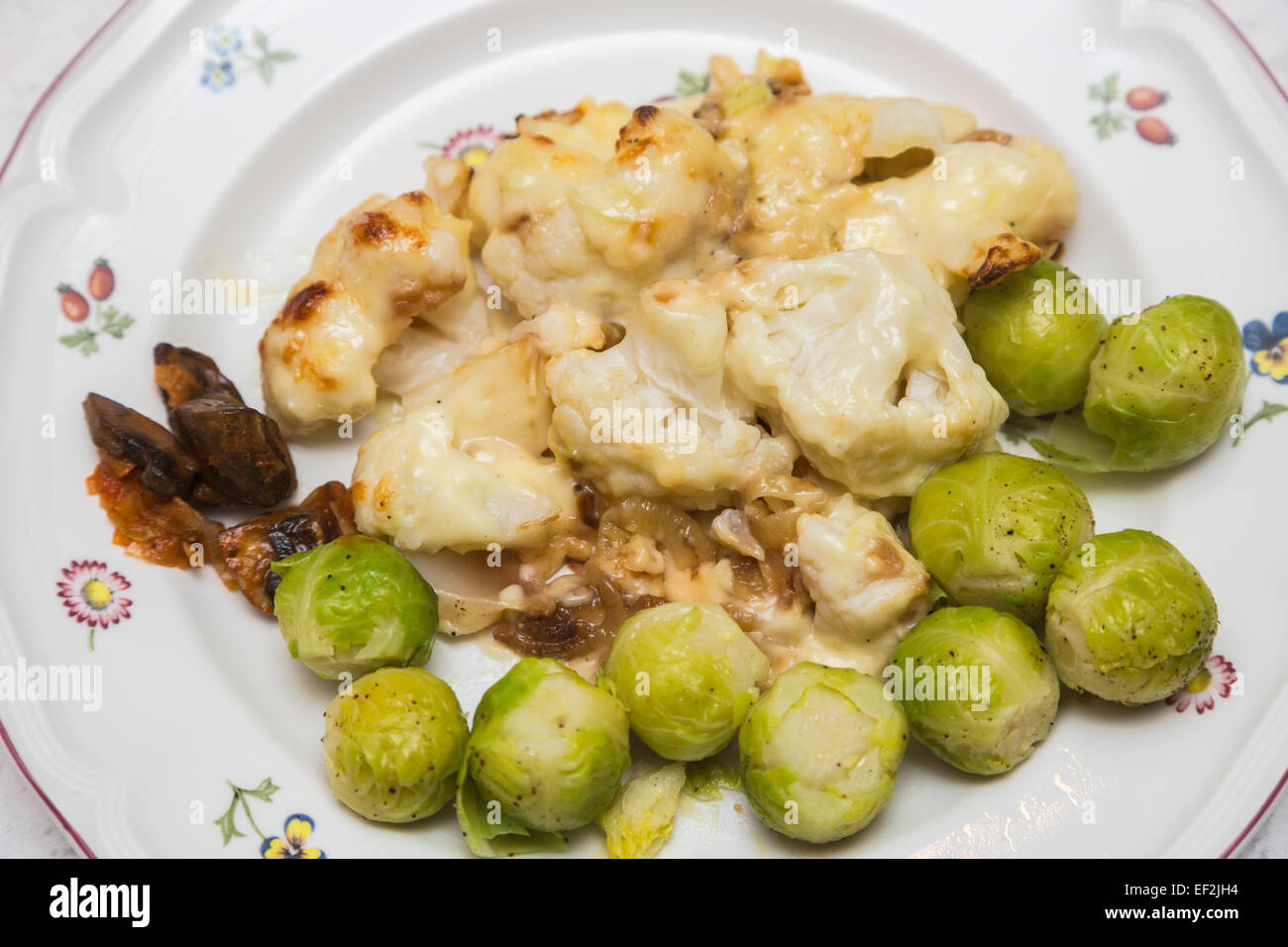 Brassica plat végétarien : chou-fleur cuit maison saine avec les choux de Bruxelles fromage servi sur une plaque blanche chine avec de petites fleurs colorées Banque D'Images