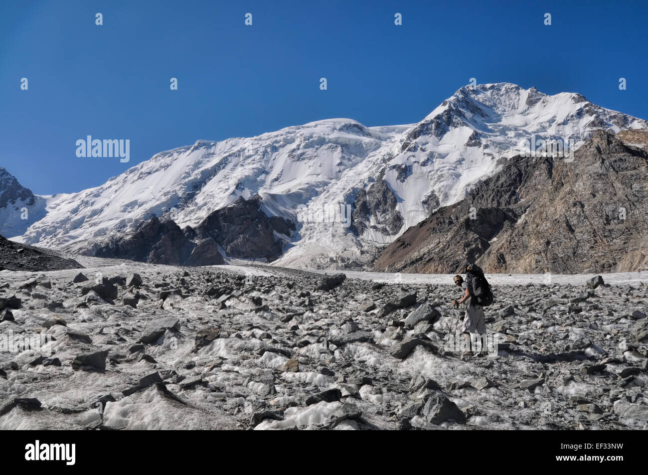 Jeune aventurier avec sac à dos sur glacier ci-dessous les plus hauts sommets de montagnes de Tian-shan occidental au Kirghizstan Banque D'Images