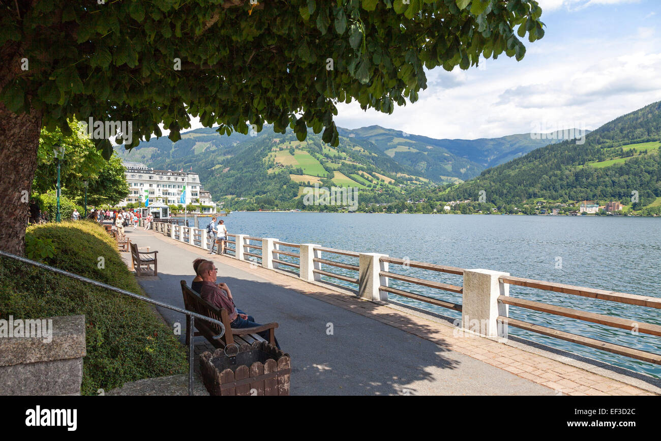 Des gens assis sur un banc sur la promenade et le lac avec les montagnes en arrière-plan à Zell am See Autriche en été Banque D'Images