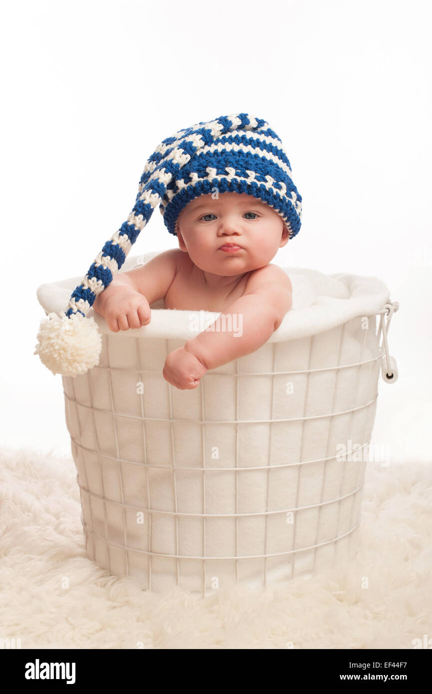 A 4 mois bébé garçon portant un chapeau bas. Il est assis dans un panier avec les poings serrés et une moue d'expression. Shot Banque D'Images