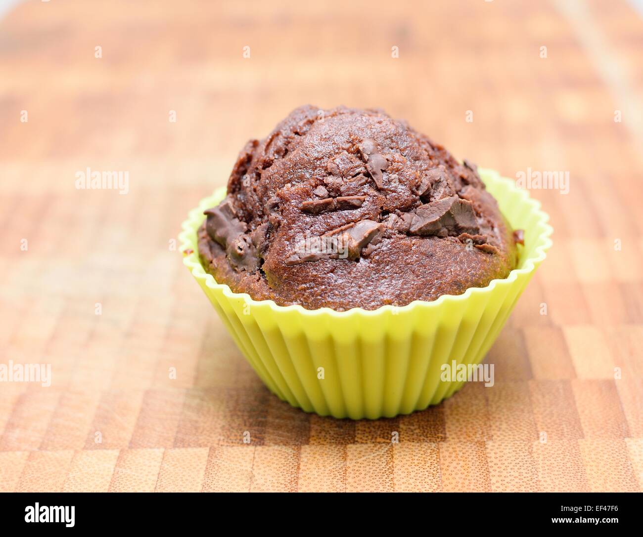 Muffin au chocolat dans la forme en silicone jaune sur une plaque de bois. Banque D'Images