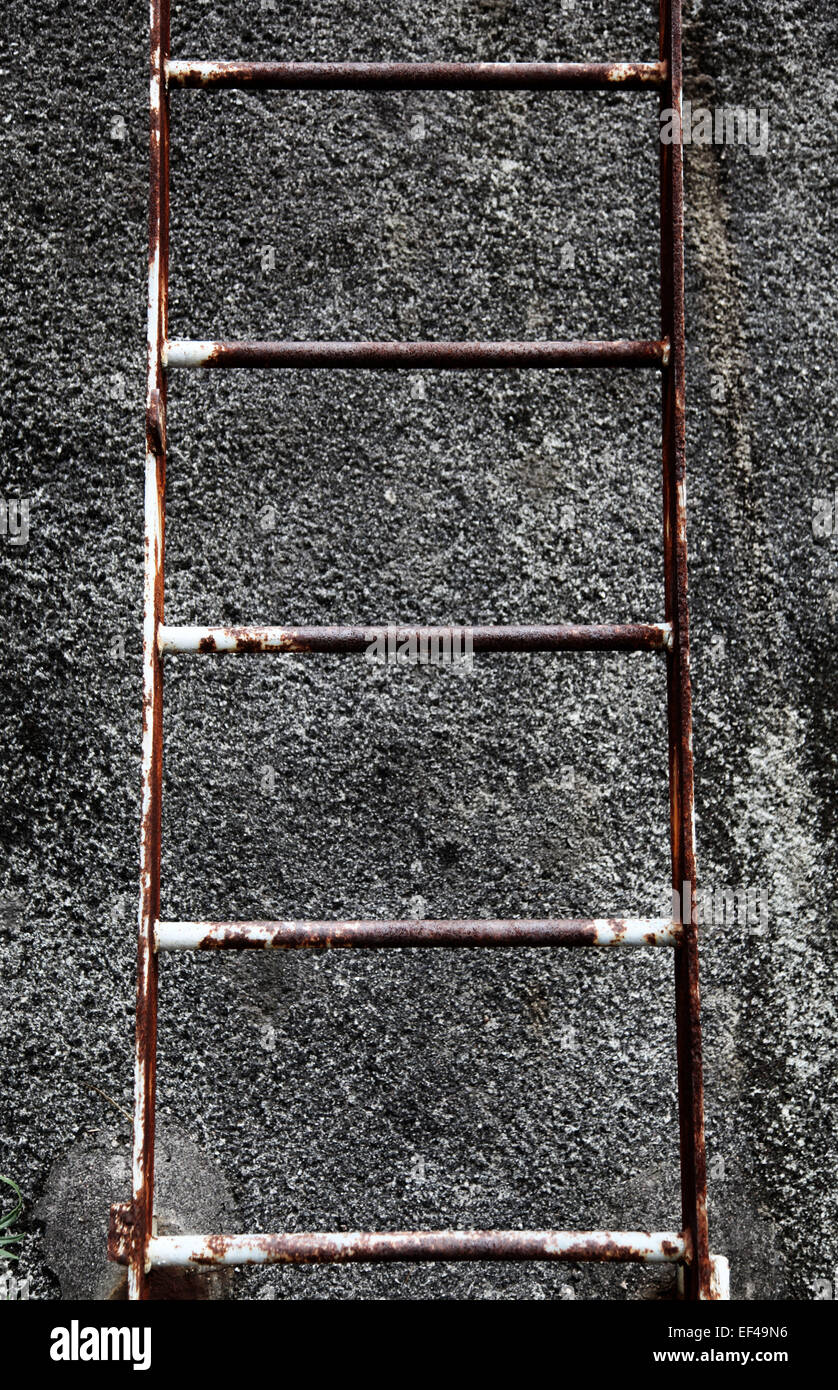 Ceci est une photo d'un détail d'une échelle d'acier rouillé qui est contre un mur de béton rugueux Banque D'Images