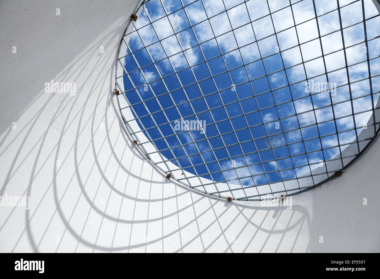 Résumé de l'intérieur blanc fragment. Blue cloudy sky derrière la fenêtre avec grille métallique ronde Banque D'Images