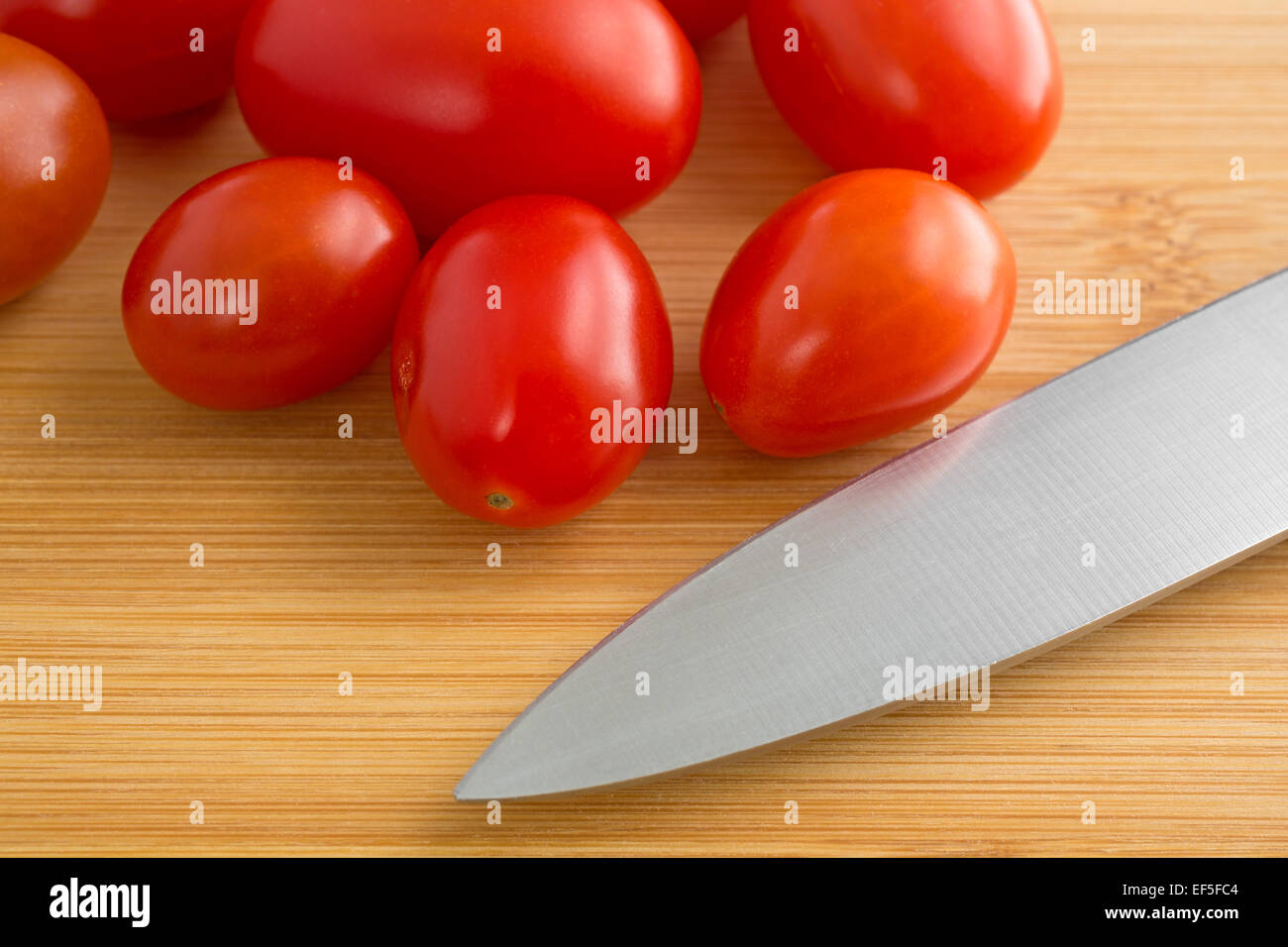 Un groupe de petites tomates raisins sur une planche à découper en bois avec un couteau pointu à l'avant-plan. Banque D'Images