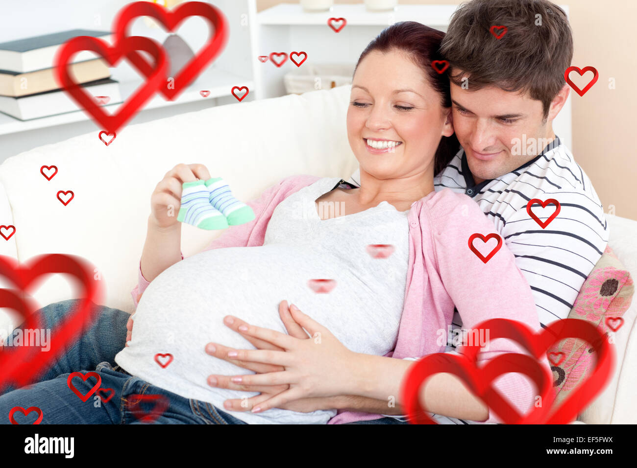 Composite image of happy pregnant woman holding baby shoes et de son mari sur un sof Banque D'Images