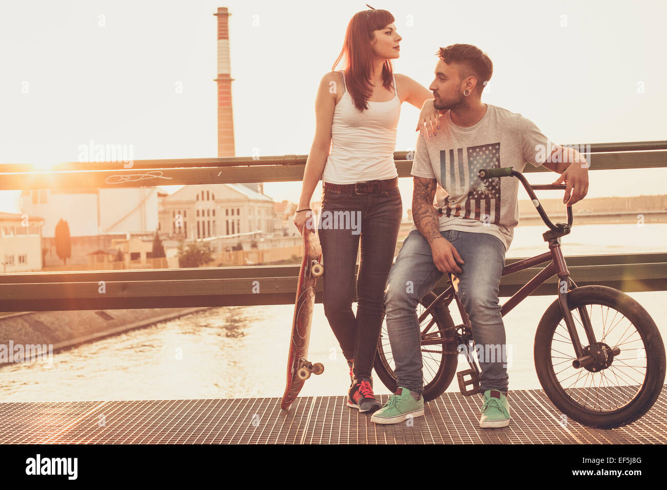 Jeune couple avec Skateboard and BMX location reposant sur bridge Banque D'Images