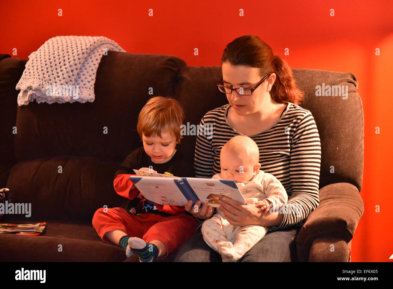 Une mère était assis sur un canapé la lecture de ses deux enfants, l'un des cinq derniers mois et l'autre deux ans et demi Banque D'Images