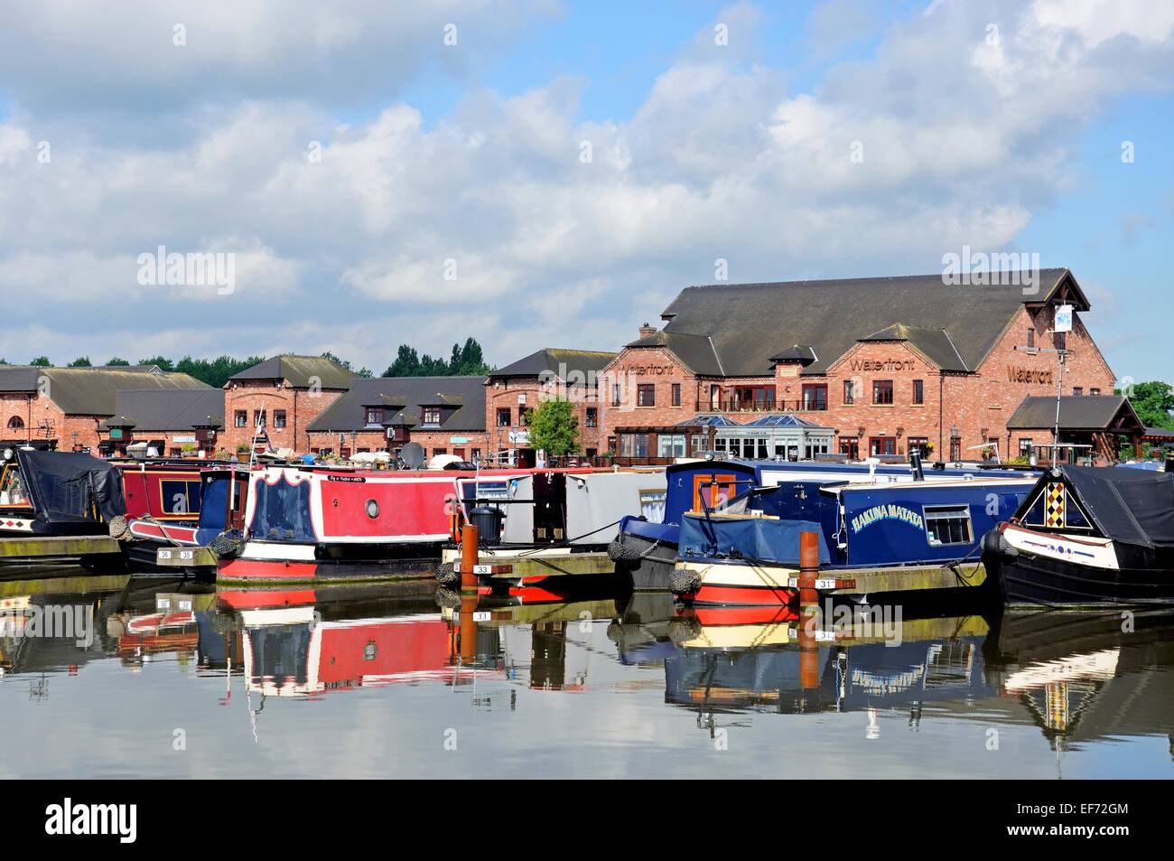 Narrowboats sur leurs amarres dans le bassin du canal, avec des magasins, bars et restaurants à l'arrière, Barton Marina, England, UK. Banque D'Images