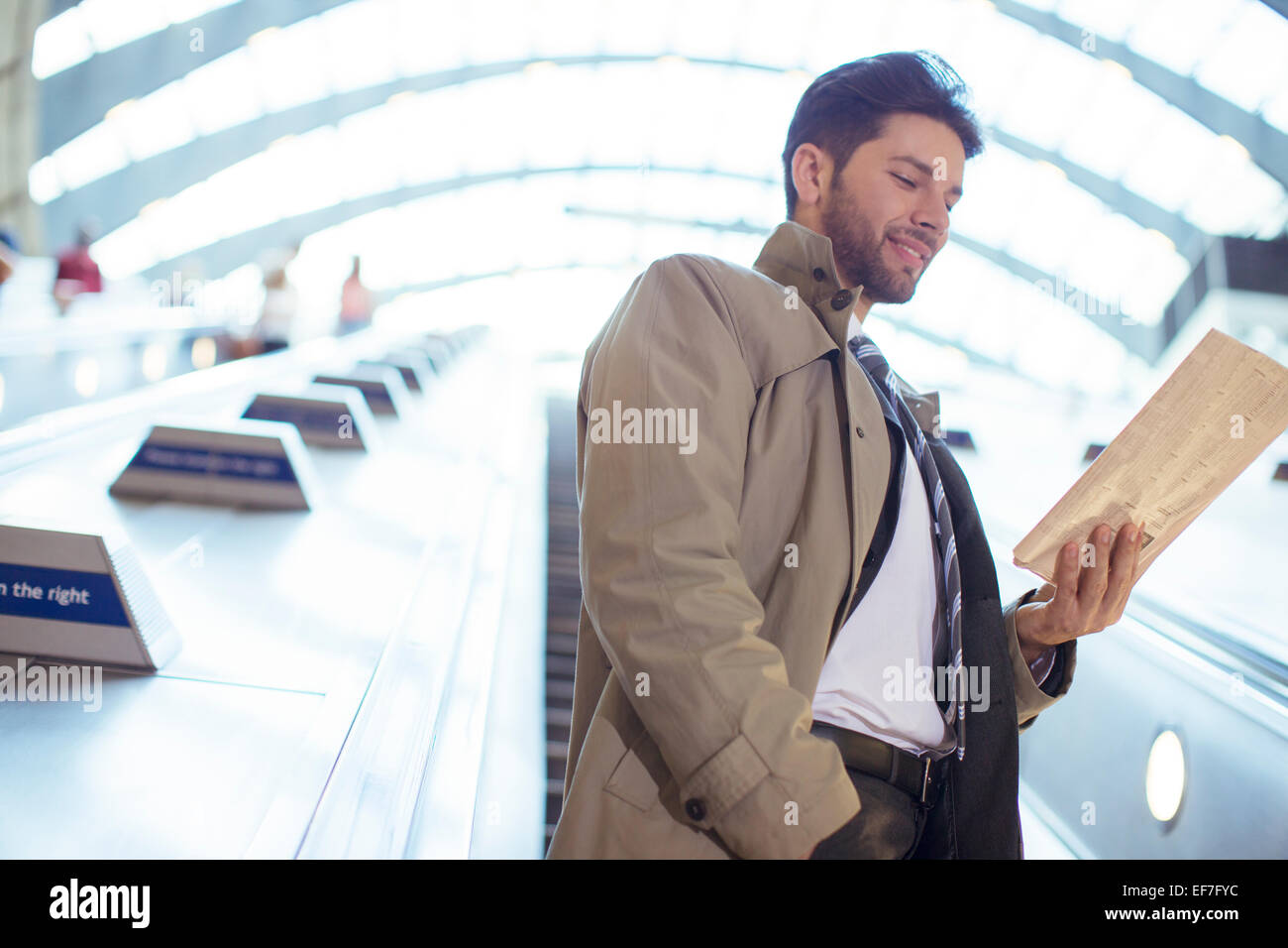 Businessman reading newspaper on escalator Banque D'Images