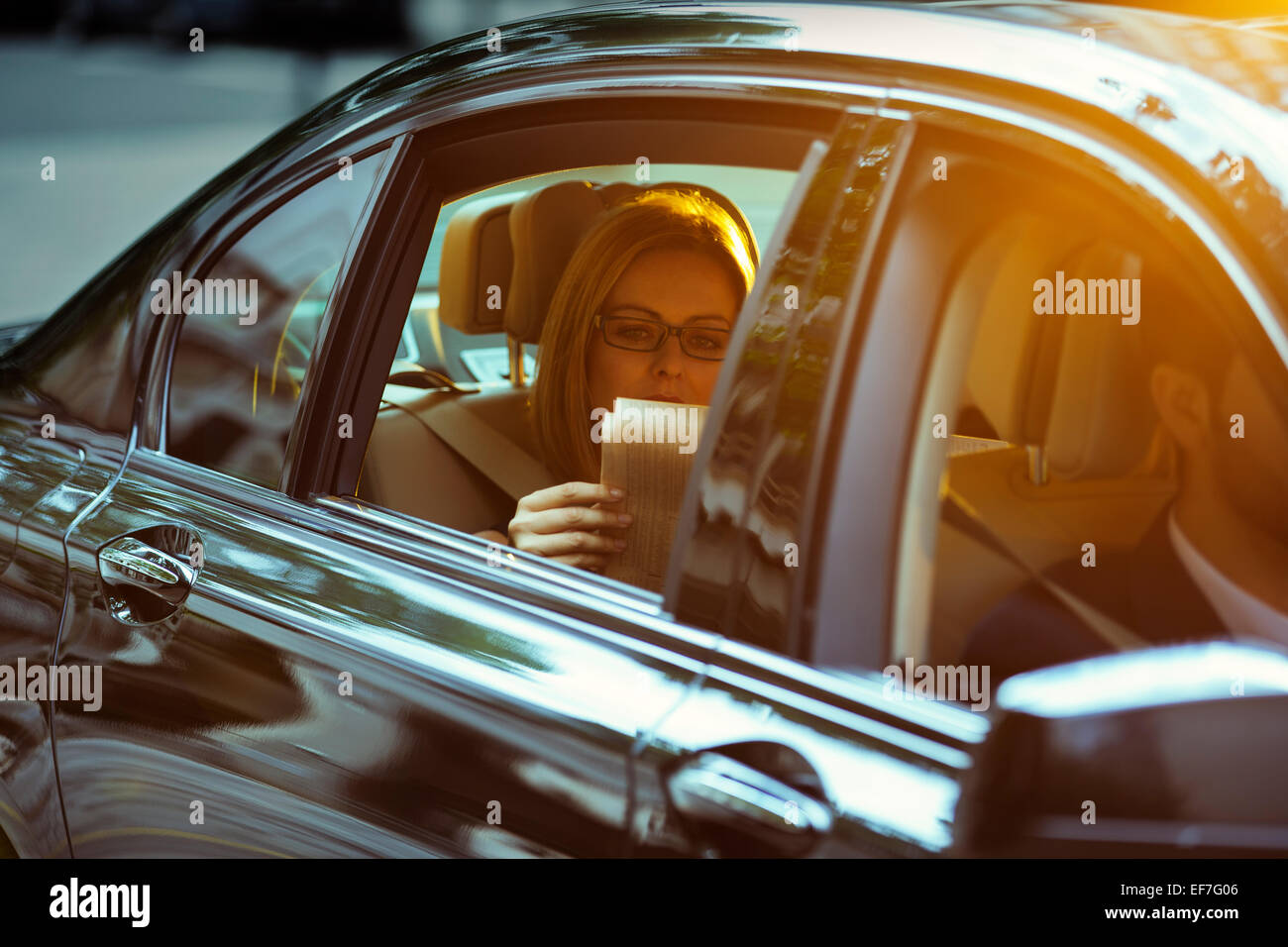 Businesswoman reading newspaper in back seat of car Banque D'Images
