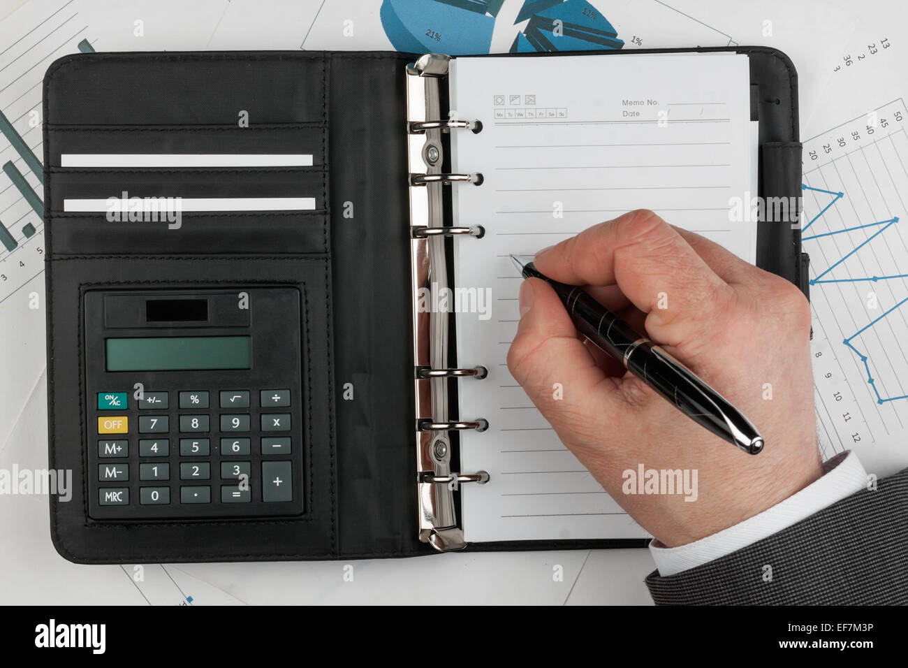 Agenda, calculatrice, stylo à la main et sur un arrière-plan de diagrammes  et graphiques Photo Stock - Alamy