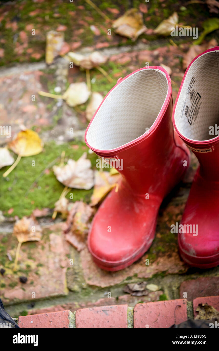 Une paire de bottes Hunter rouge sur une porte entourée de feuilles. Banque D'Images