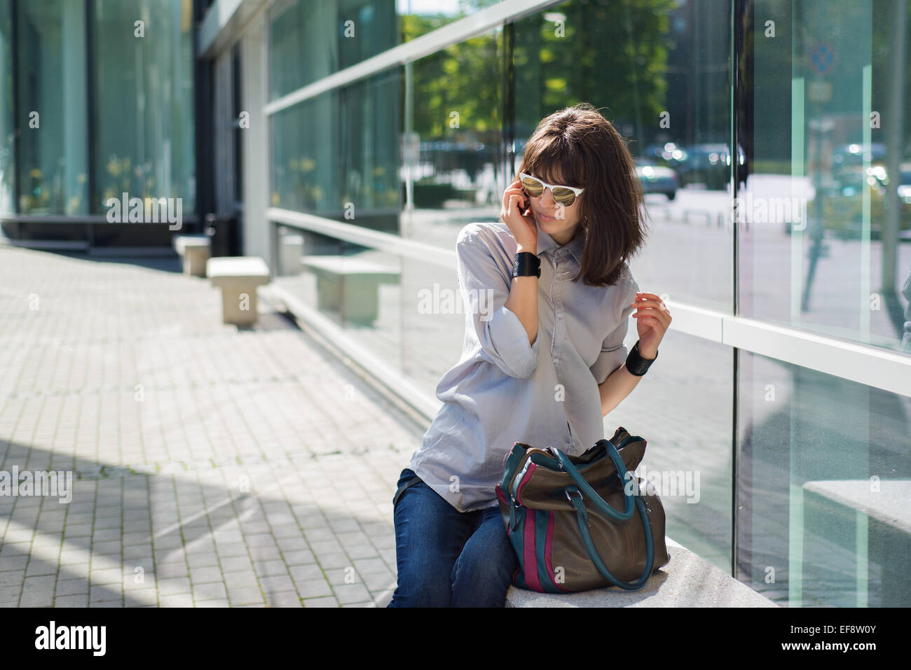 Woman sitting in street talking on mobile phone Banque D'Images