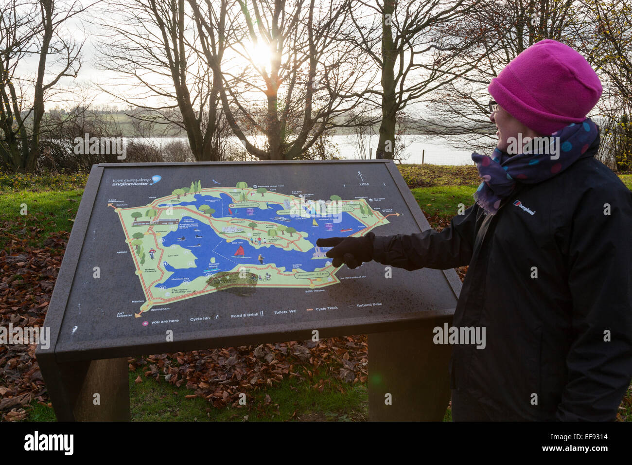 Femme dans un chapeau rose à points d'une carte touristique de Rutland Water avec le réservoir visible à travers les arbres. Banque D'Images