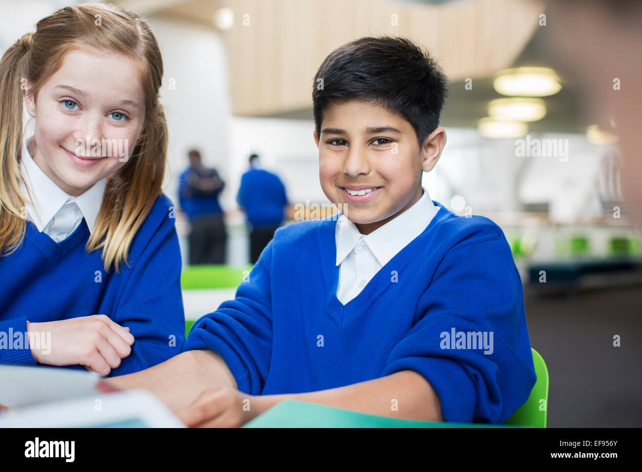 Portrait of smiling school enfants portant l'uniforme bleu sitting at desk Banque D'Images