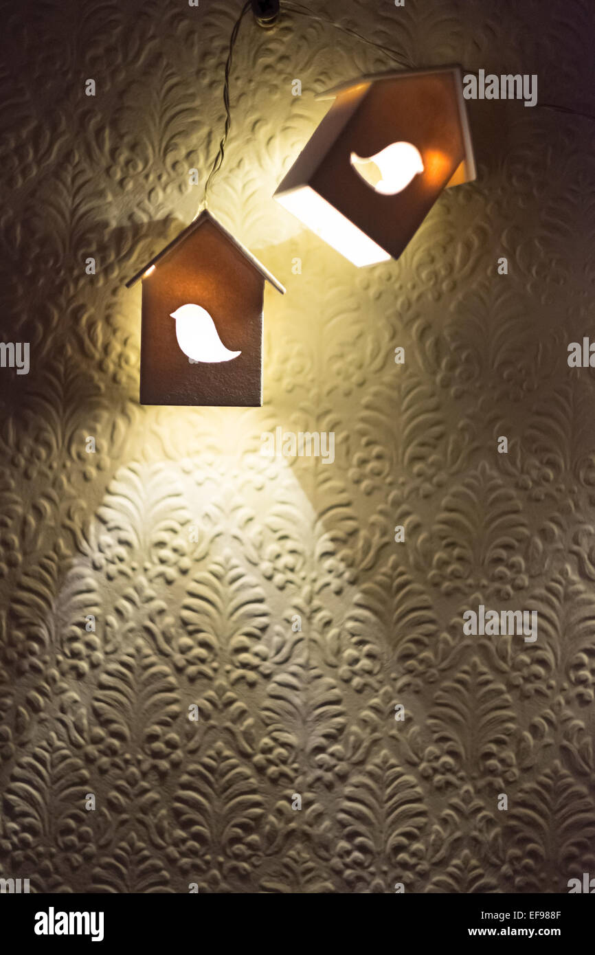 Deux petites maisons en bois avec des lampes en forme d'oiseaux découpés dans l'éclairage avant d'un mur texturé Banque D'Images